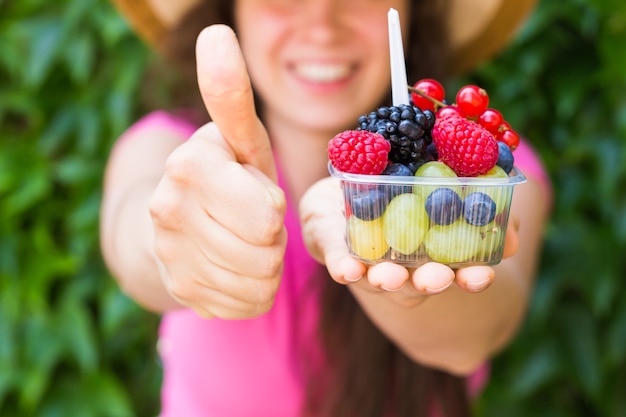 Cibo ecologico e concetto di stile di vita sano - ritratto di donna sorridente che tiene in mano le bacche e mostra il gesto del pollice in su.