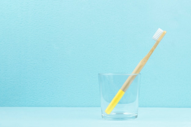 Foto spazzolino da denti di bambù ecologico in un vetro trasparente su uno sfondo blu con spazio di copia. concetto di rifiuti zero.