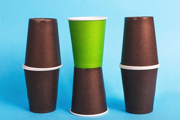 Экологичные одноразовые коричневые и зеленые бумажные стаканчики на синем фоне. Понятие экологии.