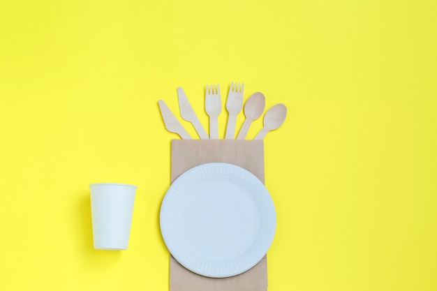 Eco-friendly disposable utensils made of bamboo wood on paper bag on yellow background.