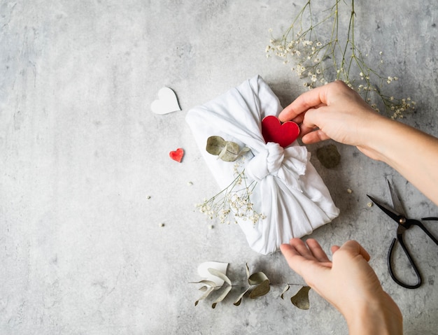 Eco-friendly fabric reusable gift packaging with Eucalyptus, white flowers and red wood heart. Valentine's day reusable sustainable gift wrapping alternative.