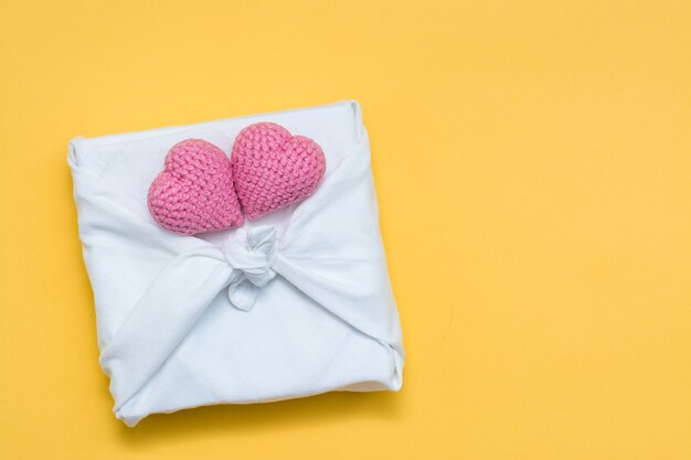 Eco friendly gift furoshiki and knitted hearts on yellow background. Copy space. Top view
