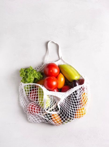 Eco-friendly mesh bag with vegetables on a gray surface