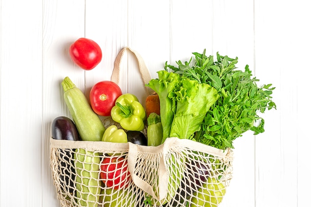 Eco friendly mesh shop bag with organic green vegetables on white wood