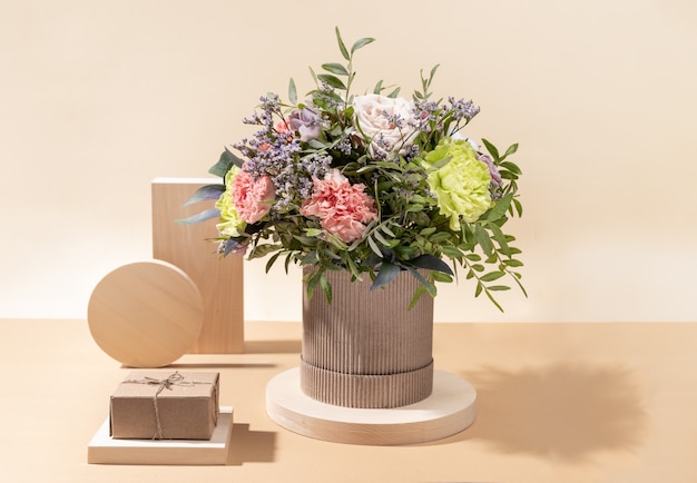 Eco friendly minimal monochrome composition with flowers bouquet and wooden stands of different shape with DIY gift box on beige background with shadows.