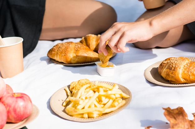 Eco-friendly picnic for schoolchildren in the park. children's
hand dips nuggets in cheese sauce at a picnic in an autumn sunny
park. back to school concept