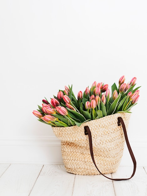 Borsa shopping ecologica tessuta con tulipani di fronte a uno sfondo bianco muro