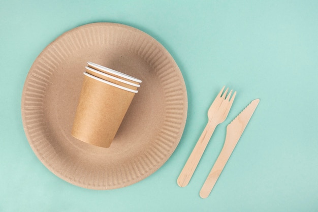 Photo eco-friendly tableware on a blue background, paper plates and glasses, wooden forks and nomes, top view