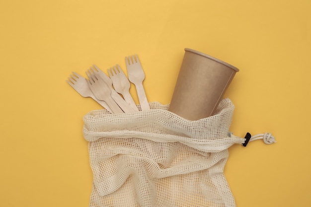 Eco katoenen tas met houten lepels en kartonnen beker op gele achtergrond. milieuvriendelijk concept. bovenaanzicht