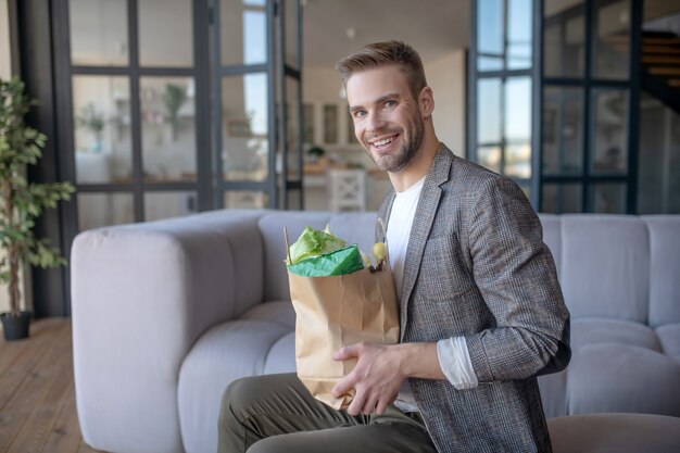 Stile di vita ecologico. un bell'uomo sorridente in possesso di un pacchetto di verdure fresche