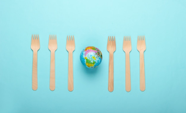 Eco still life. Plastic free concept. Globe with wooden forks on blue background. Top view