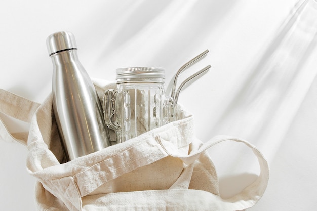 Eco-tas in natuurlijke kleur met herbruikbare metalen waterfles, glazen pot en rietje. zero waste.