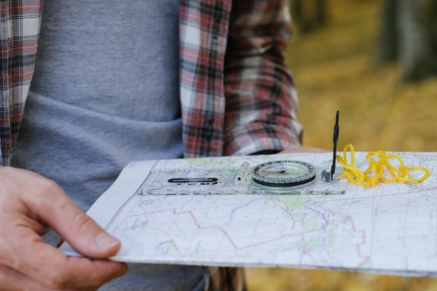 Photo eco tourism cropped shot of male traveler holding compass and map to explore country blur autumn foliage background