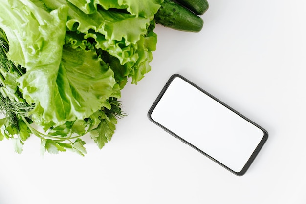 Eco vegetables and smartphone mockup on white table top view Closeup of mobile phone with blank white screen for advertising and garden organic food lettuce cucumbers