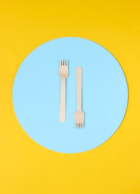 Eco-vriendelijke houten vorken op gele achtergrond met blauwe cirkel.