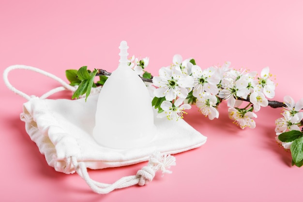 Eco white menstrual cup and cotton bag on a pink background spring cherry tree branches with white flowers Ecology and recycling concept zero waste Women39s hygiene menstruation critical days