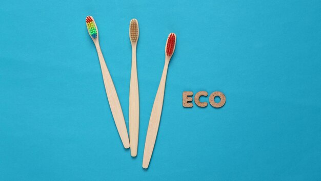 Ecofriendly bamboo toothbrushes and word eco on blue background top view