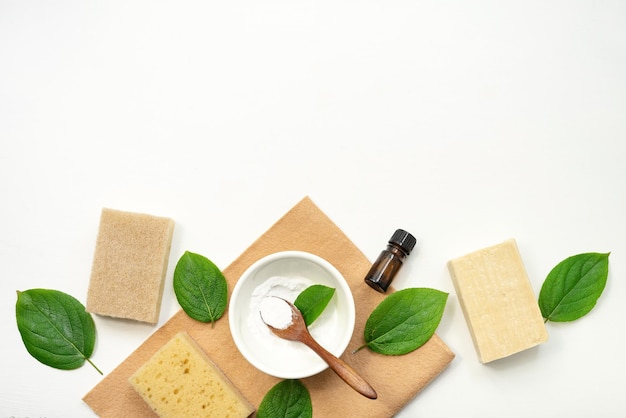 Ecofriendly cleaning products and dishwashing detergents on a white background with green leaves Coconut sponges baking soda natural laundry soap a bottle of essential oil or vinegar Zero waste