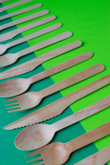 Ecofriendly disposable dishes made of bamboo wood and paper on a green background draped spoons forks knives bamboo bowls with paper cups abstract