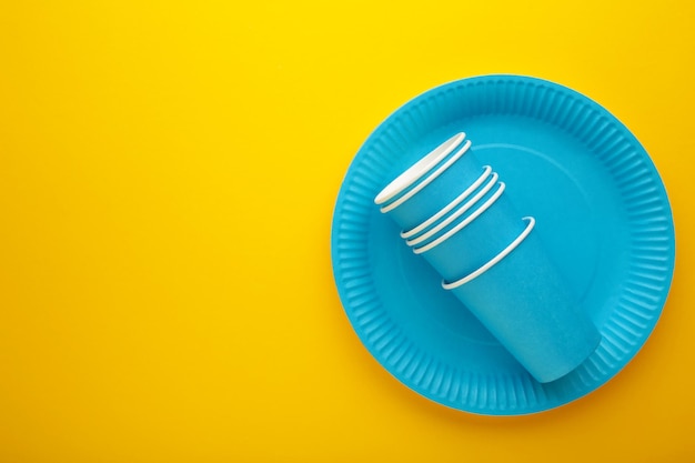 Ecofriendly disposable utensils made of craft paper on yellow background Blue plates and paper cups