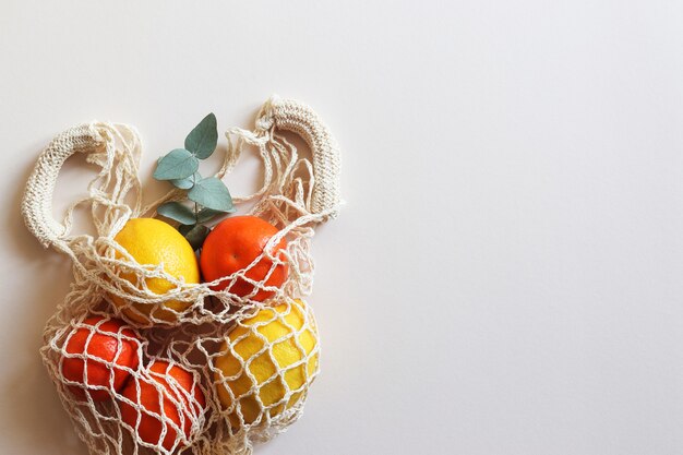 Ecofriendly string bag with lemons and tangerines on light beige table