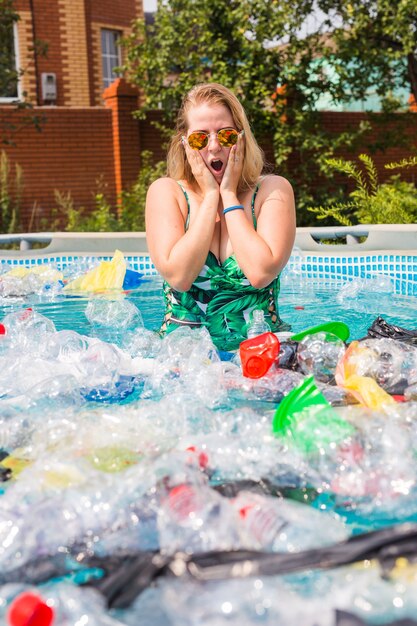 Ecologie, plastic afval, ecologische noodsituatie en watervervuiling - Geschokte vrouw in een vies zwembad.