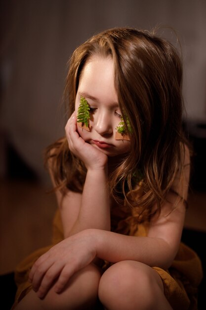 Ecology concept, portrait of a little pensive girl with fern sprigs pasted with plasters on her cheeks.