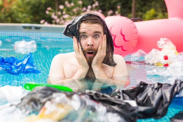 Ecology, plastic trash, environmental emergency and water pollution - shocked man swim in a dirty swimming pool.