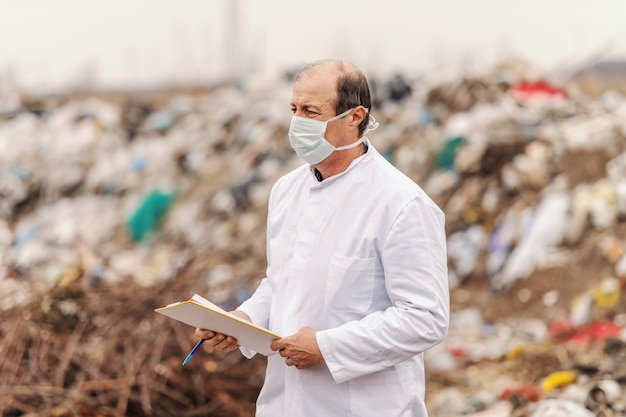 Ecoloog in wit uniform en masker op het gezicht met klembord en evaluatie van schade