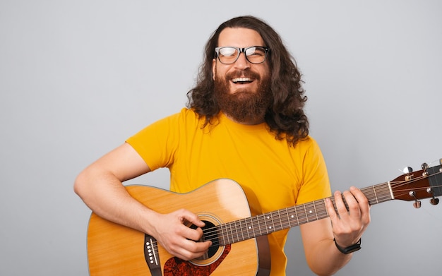 Premium Photo | Ecstatic bearded man wearing yellow t shirt with long hair  is playing on an acoustic guitar studio photo over grey background