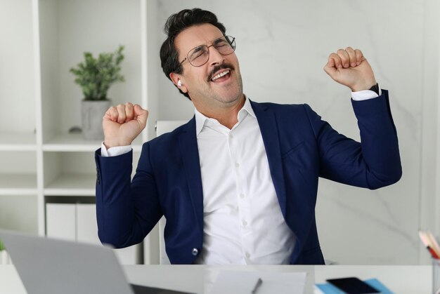 Foto un uomo d'affari estatico in abito blu con gli occhi chiusi e i pugni pompati celebra una vittoria