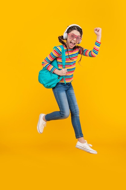 Ecstatic energetic school girl jumping and making winning gesture yellow background School education