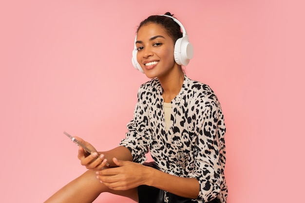 Ecstatic woman with pleasue listening lovely music on pink background Holding mobyle phone Wearing stylish blouse and leather skirt