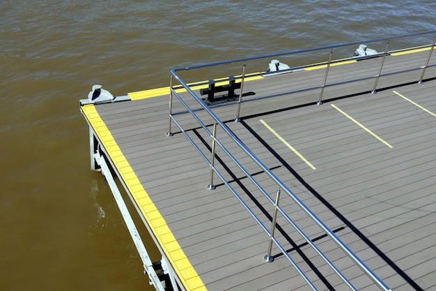黄色いマーキングのある桟橋の端と、水面近くに手すりを備えた金属製の手すりフェンス