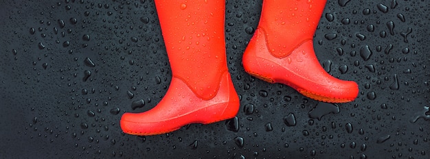 The edges of the orange rain boots are on a wet wet surface covered with raindrops.