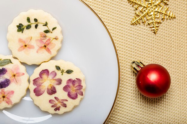 Biscotti di fiori commestibili con ornamenti di fiocchi di neve di natale su sfondo di lamiera metallica dorata.