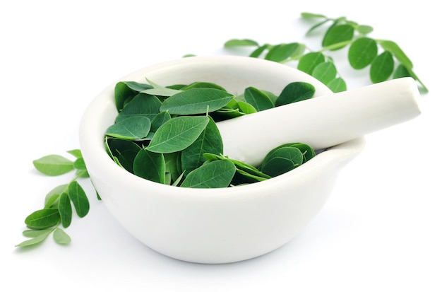 Edible moringa leaves with mortar and pestle over white background