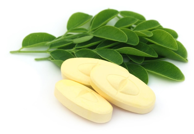 Edible moringa leaves with pills over white