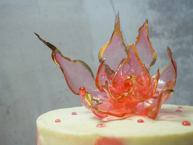 An edible red isomalt flower on top of a cake on a light concrete background