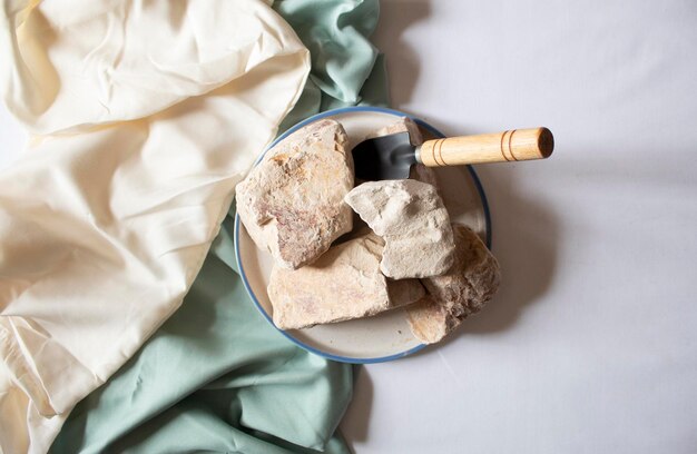 Edible white clay stones on round plate with a small shovel on a white background