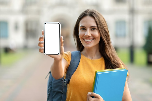 Educatieve advertentie die jonge vrouwelijke student glimlacht die het lege smartphonescherm demonstreert bij de camera