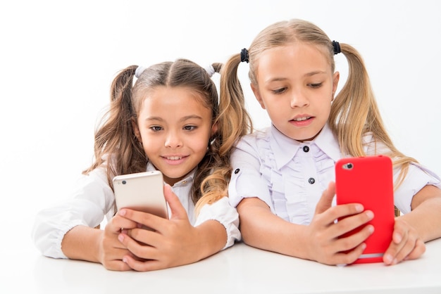 Educatieve toepassing Online levensconcept Schoolmeisjes schattige leerlingen gebruiken smartphones groot diagonaal scherm controleer sociale netwerken Stuur bericht vriend Online communicatieberichten Speltoepassing