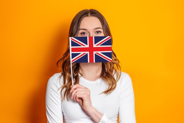 Education abroad. Female student cover her face with British flag isolated over orange background