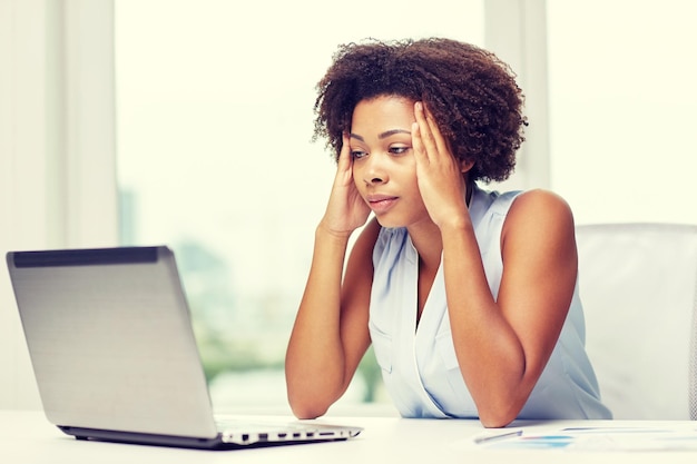 education, business, fail and technology concept - african american businesswoman or student with laptop computer and papers at office