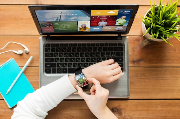 education, business, people, mass media and technology concept - close up of woman with smart watch and laptop computer on wooden table with internet application on screens