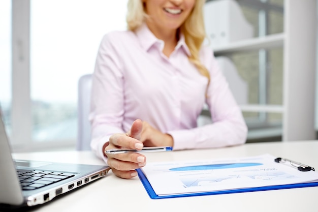 education, business, people and technology concept - close up of smiling businesswoman with laptop computer and papers sitting in office