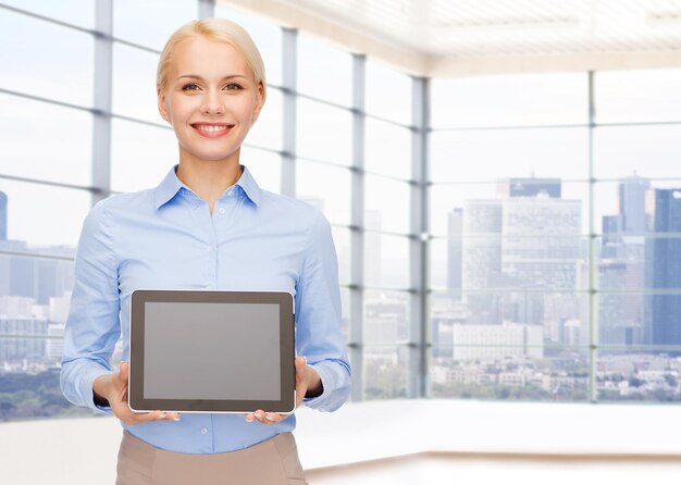 Photo education, business and technology concept - smiling businesswoman or student showing tablet pc computer blank screen over office room or new apartment background