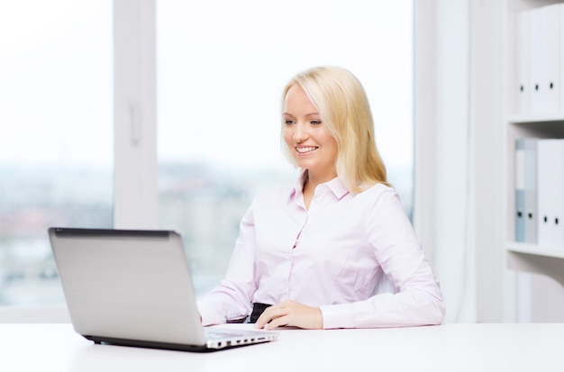 education, business and technology concept - smiling businesswoman or student with laptop computer in office