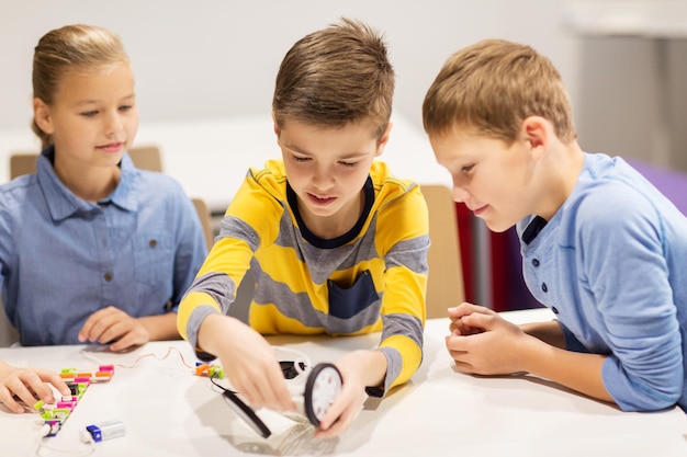 education, children, technology, science and people concept - group of happy kids building robots at robotics school lesson