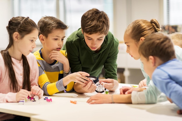 education, children, technology, science and people concept - group of happy kids building robots at robotics school lesson